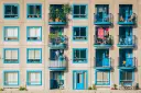 Elegancka loggia i balkon z niebieskimi ramami okiennymi, pełne zieleni i suszącego się prania, tworzą kolorowy wzór na fasadzie budynku.