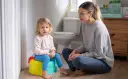Mama uczy dziecko, jak nauczyć dziecko korzystać z nocnika. Maluch siedzi na kolorowym nocniku, mama siedzi obok.