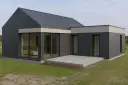 Nowoczesna dobudówka do starego domu, z dużymi przeszkleniami i grafitową elewacją. Projekty takich rozbudów to świetny sposób na odświeżenie wyglądu.