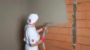 Pracownik nakłada tynk cementowo-wapienny na ścianę z pustaków ceramicznych. Sprawdź atrakcyjną tynki cementowo wapienne cenę!