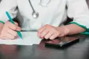 Lekarz pisze zwolnienie, zastanawiając się, na ile lekarz może wystawić L4 jednorazowo. Obok leży telefon.