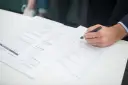 Ręka klienta podpisuje dokumenty ubezpieczeniowe. Agent ubezpieczeniowy czeka na zakończenie formalności.