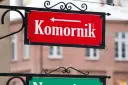 Czerwona tablica z napisem "Komornik" i strzałką w lewo. W tle budynek, może to być miejsce, gdzie zasiłek chorobowy jest zagrożony przez komornika.