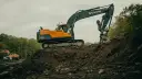 Pomarańczowo-czarna koparka Volvo EC220DL pracuje na budowie. Operator koparki gąsienicowej zarabia dobrze, wykonując ciężką pracę.
