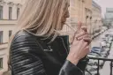 Kobieta w skórzanej kurtce zapala papierosa na balkonie, zastanawiając się, czy można palić na balkonie.