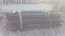 Stos czarnych, metalowych elementów naczepy z pasami transportowymi.