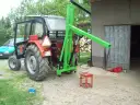 Czerwony traktor z zamontowanym zielonym ładowaczem TUZ przed budynkiem gospodarczym.