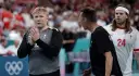 Trzech zawodników Danii w piłce ręcznej na boisku. Jeden z nich, w szarej koszulce, klaszcze.