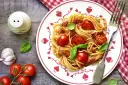 Makaron spaghetti z sosem pomidorowym, pomidorkami koktajlowymi i bazylią na talerzu.