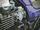 Szczegółowy widok gaźnika motocyklowego, kluczowego elementu układu dolotowego, z widocznymi przewodami i częściami silnika.