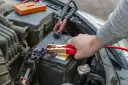 Ręka podłącza kable rozruchowe do akumulatora samochodowego.