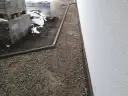 Wykonano opaskę wokół domu z kruszywa, obok ułożone palety z materiałami budowlanymi.