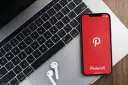 Telefon z aplikacją Pinterest obok klawiatury laptopa i słuchawek.