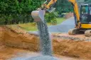Koparka wysypuje tłuczeń do wykopu, tworząc fundament pod przyszłą drogę.