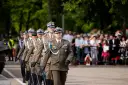 Tomasz Zaręba w mundurze maszeruje w defiladzie wojskowej. W tle widzowie obserwują uroczystość.