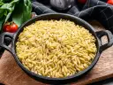 Makaron orzo w czarnej patelni, obok pomidorów i ziół. Wygląda jak ryż, ale to pyszny makaron!