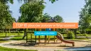 Kolorowy plac zabaw z piaskownicą i zjeżdżalnią, otoczony zielenią.
