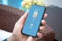Dłoń trzyma smartfon z wyświetloną grafiką porównującą tradycyjną kartę SIM z technologią eSIM.