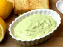 Pyszna pasta z awokado i jajka w białej miseczce, obok połówki cytryny i tostów. Idealna na śniadanie.