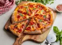 Pikantna pizza diavola z pepperoni i bazylią, pokrojona na kawałki, leży na drewnianej desce. Obok sos i nóż do pizzy.