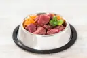 Un cuenco de metal lleno de trozos de carne cruda y zanahoria rallada, perfecto para una dieta BARF perros casera.