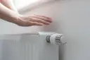 Dłoń nad grzejnikiem, sprawdzająca ciepło. Rozpoczyna się sezon grzewczy, czas na komfortowe ogrzewanie.