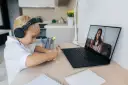 Chłopiec w słuchawkach uczy się zdalnie, patrząc na ekran laptopa z nauczycielem.
