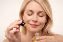 Kobieta z zamkniętymi oczami aplikuje serum z **retinolem**, dbając o skórę, by uniknąć efektów **solarium**.