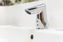 Elegancka bateria umywalkowa z korkiem, wykonana z chromowanego metalu, lśni na białej ceramice.