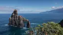 Skaliste formacje w morzu, wybrzeże z roślinnością i góry w tle.