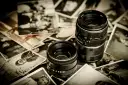 Dwa obiektywy aparatów leżą na starych, czarno-białych fotografiach.