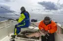 Dwóch wędkarzy na łodzi, jeden przygotowuje rybę, drugi łowi. Widać kilka sporych sztuk ryb w skrzynce. Jaka wędka na spinning?
