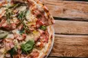 Pyszna pizza carbonara z chrupiącym boczkiem i rukolą, podana na drewnianym blacie.