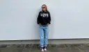 Dziewczyna w czarnej bluzie z kapturem i jeansach, idealny outfit, jak się ubrać na koncert hip hopowy.