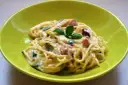 Spaghetti carbonara ze śmietaną, podane w zielonej misce, udekorowane bazylią. Pyszny przepis na klasyczne danie.