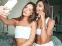 Dwie dziewczyny, obie w białych topach i z płatkami pod oczami, robią sobie selfie. Jedna z nich trzyma telefon. To idealny moment dla każdej it girl na zadbanie o siebie.