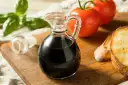 Szklana karafka z ciemnym, gęstym sosem balsamicznym, obok pomidorów, bazylii i grzanek. Idealny dodatek do sałatek.