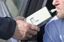 Badanie alkomatem. Kierowca dmucha, by sprawdzić, na ile zabierają prawo jazdy za alkohol 1 promil.