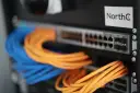Netzwerkschrank mit blauen und orangen Kabeln, die an einen Switch angeschlossen sind.