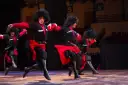 Tancerze baletu gruzińskiego Sukhishvili w tradycyjnych strojach z czarnymi czubami i czerwonymi akcentami wykonują dynamiczny taniec na scenie.