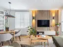 Przytulny salon inspiracje: drewniana ściana z TV, okrągły stół z krzesłami, rośliny i stylowe oświetlenie tworzą ciepłą atmosferę.