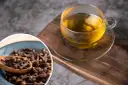 Napar z goździków przepis: aromatyczna herbata w szklance i miseczka pełna goździków na drewnianej desce.