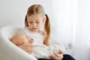 Starsza siostra delikatnie trzyma noworodka, ucząc się jak przygotować dziecko na rodzeństwo.