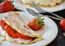 Słodki omlet z truskawkami i bitą śmietaną, posypany cukrem pudrem. Idealny przepis na omlet na słodko.