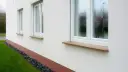 Eleganckie, kamienne parapety przy białym domu. Zastanawiasz się, jak przedłużyć parapet? Ten przykład pokazuje, jak estetycznie można to zrobić.
