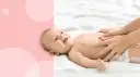 Uśmiechnięty noworodek się pręży i robi czerwony, gdy mama delikatnie masuje mu brzuszek.