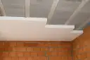 Białe płyty styropianowe montowane do betonowego stropu, przygotowanie do tynkowania sufitu. Widoczne ceglane ściany.