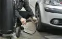 Un homme gonfle un pneu de voiture avec un manomètre et un compresseur.