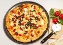 Pyszna pizza z serka wiejskiego, pomidorkami koktajlowymi i bazylią. Obok leży krajalnica do pizzy i świeże pomidory.