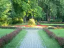 Kamienista ścieżka prowadzi przez park z kwitnącymi rabatami kwiatowymi i zielenią.